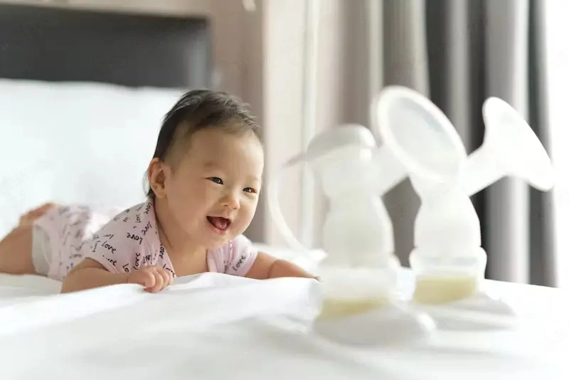 What Are The Different Types Of Breast Pump? Breast milk in milk pump's bottles on the bed with selective focus on smiling crawling baby