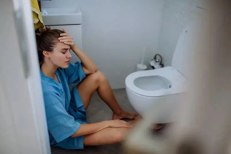 What Are Early Pregnancy Symptoms? A young pregnant woman sitting on floor near toilet.