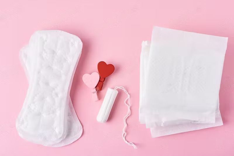 Menorrhagia Causes, Symptoms and Risk Factors - Sanitary pad, menstrual tampon and wooden red heart on pink background