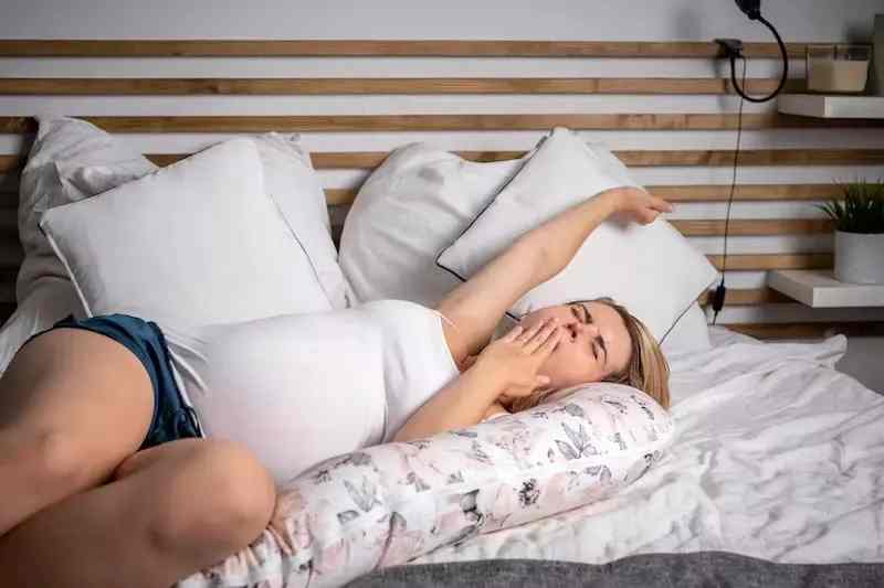 a pregnant woman having trouble sleeping, surrounded by pillows