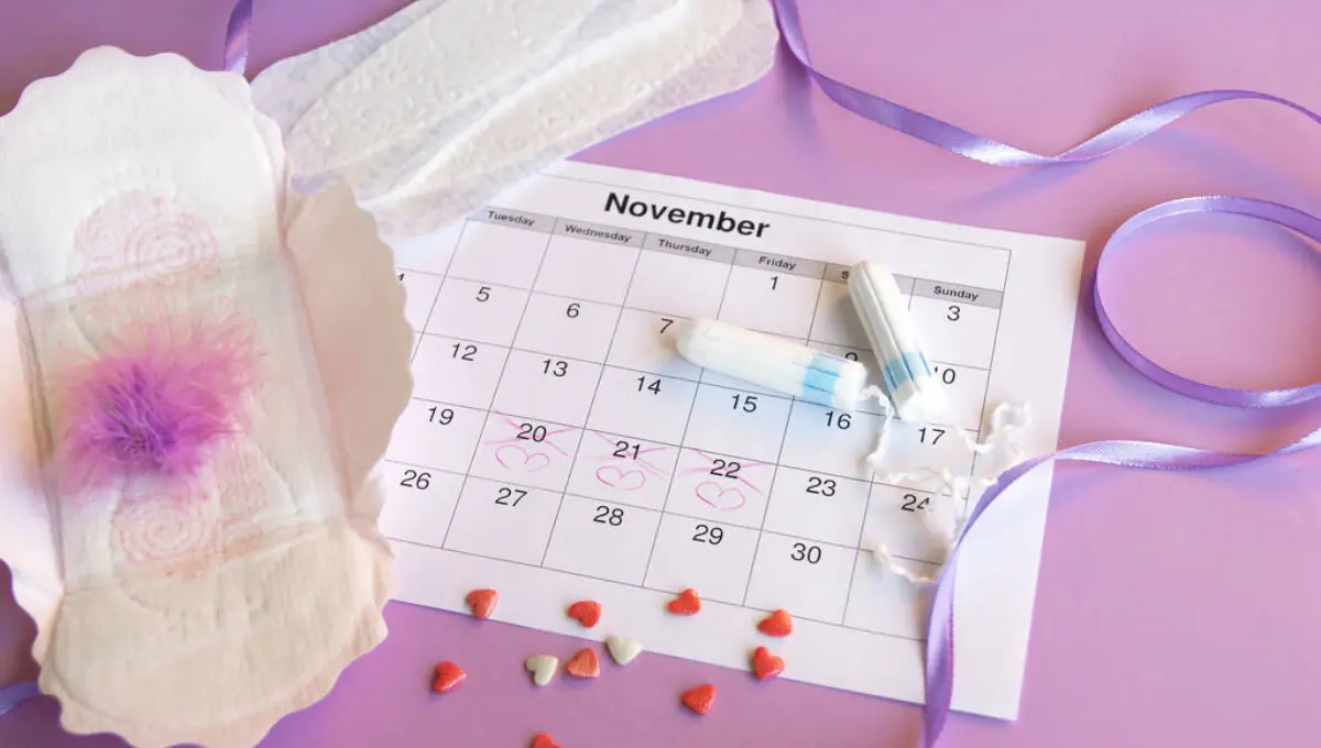 Menstrual pads and tampons on menstruation period calendar on lilac background