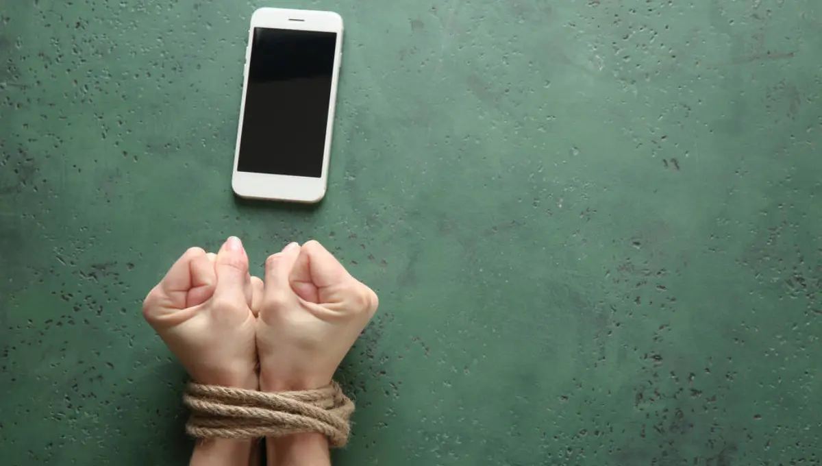 Woman with tied hands and mobile phone on color background