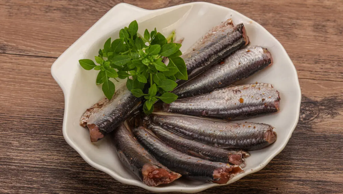 Anchovies fish snack in the bowl served with basil leaves