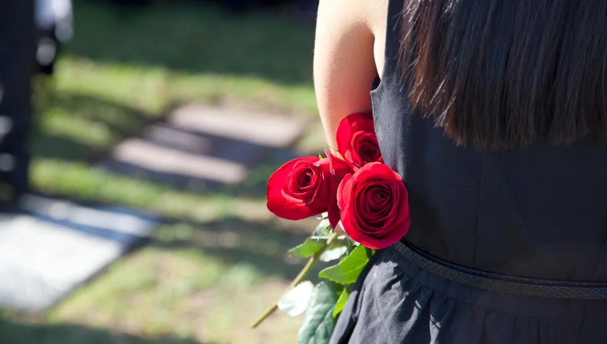 a pregnant woman holding a rose in her hand with her face turned other side standing in a cementary, attending a funeral.