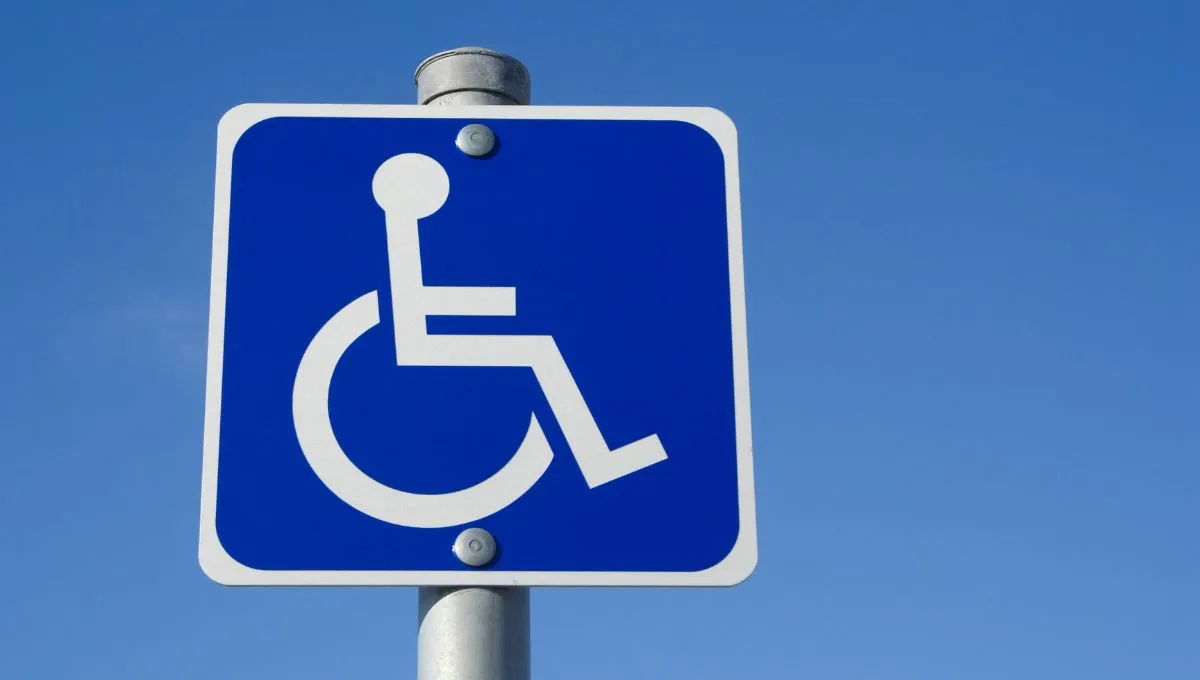 handicap parking sign on the top of a pole with blue sky in the background.