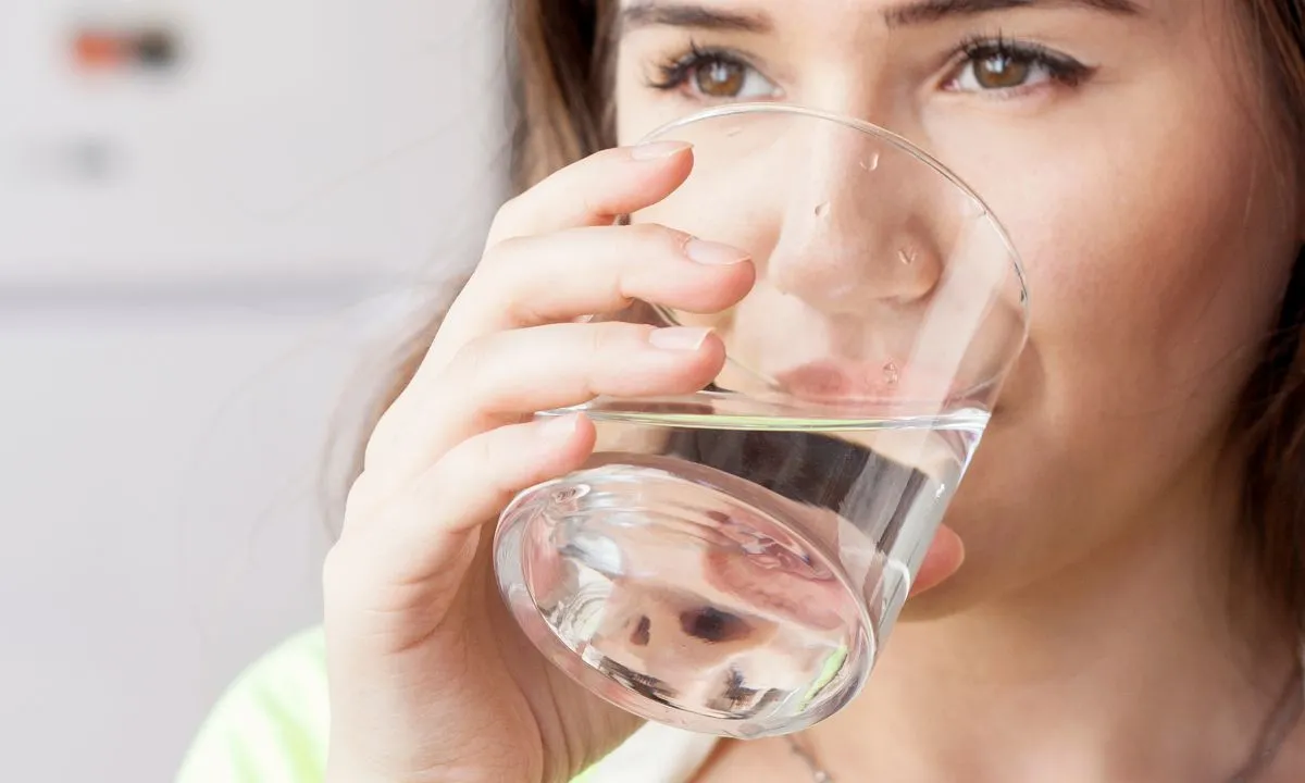 a pregnant woman drinking water from a glass to keep herself hydrated.