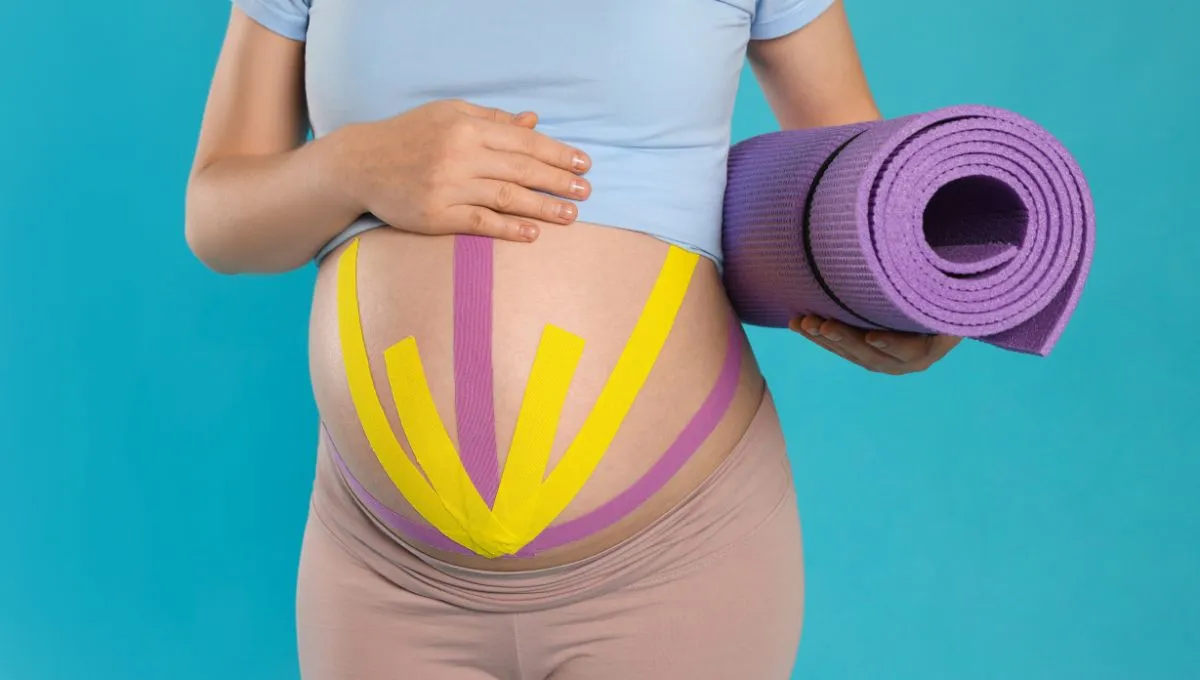 a pregnant woman with kinesio tapes on her abdomen and holding an exercise mattress in her hand. 